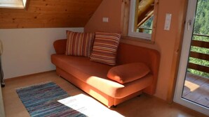 A cozy room with a wooden ceiling, a sofa with striped cushions, a small rug, and a window with a view of greenery.