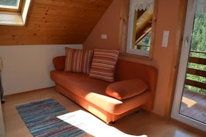 A cozy room with a wooden ceiling, a sofa with striped cushions, a small rug, and a window with a view of greenery.