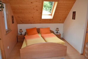 Une petite chambre à coucher accueillante, avec un plafond en pente, un puits de lumière, un lit avec une literie orange, deux tables de chevet avec des lampes et un tableau encadré au mur.