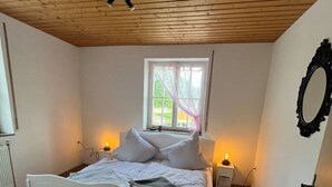 Une chambre avec un plafond en bois, un lit avec une literie blanche, une fenêtre avec des rideaux, des lampes de chevet et un miroir fixé au mur.