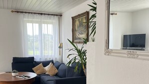 Un salon avec un canapé bleu foncé, une table basse ronde en bois, un buffet blanc orné d’un tableau encadré et un grand miroir au mur.