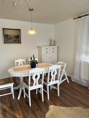 A dining area with a round table, white chairs, a potted plant, a white cabinet, and a ceiling light. - Apartment 'Ferienwohnung Modelshauser Mühle' with Wi-Fi (Laugna - Bocksberg)