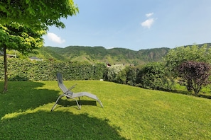 Un'area erbosa all'aperto con una sedia in metallo, un albero e vista su un paesaggio collinare.