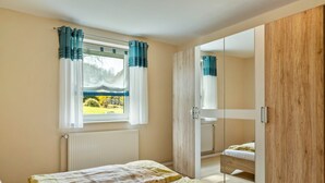 A bedroom with a bed, a window with curtains, a radiator, and a wooden wardrobe.