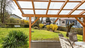 A covered patio area with a wooden pergola, a wicker sofa, and a dining table with chairs.