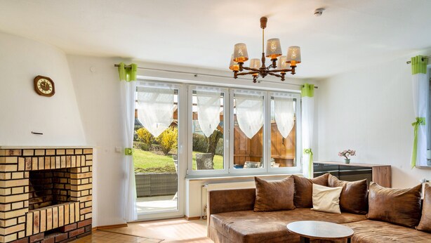 A living room with a brick fireplace, a brown sofa, a round table, and a chandelier.