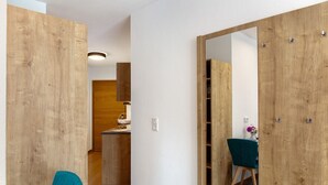Un interior moderno con paredes de madera, una zona de comedor con sillas azul verdosas y una cocina a la vista.
