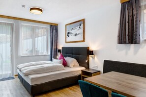 A hotel room with a bed, bedside table, lamp, and a dining table.
