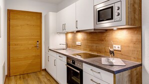 Una cocina moderna con armarios blancos, horno empotrado, microondas y puerta de madera.