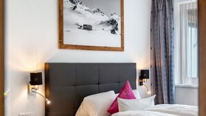 Habitación de hotel con cama, mesita de noche, lámpara de pared, un cuadro y ventana con cortinas.