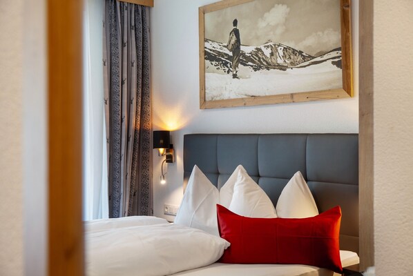 A hotel room with a bed, a headboard, a wall-mounted picture, and a nightstand with a lamp.