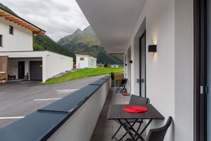 A balcony with a table and chairs, a view of a mountain, and a building with a white facade.