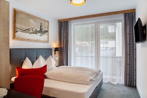 A hotel room with a bed, a red chair, a painting, a television, and a view through the window.