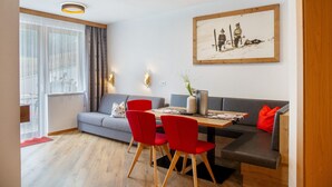 Un salon moderne avec un canapé, une table à manger et des chaises, un tableau accroché au mur et une grande fenêtre avec des rideaux.