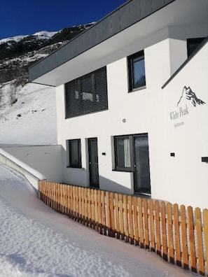Un bâtiment moderne à la façade blanche, orné d’un logo représentant une montagne et entouré d’une clôture en bois.