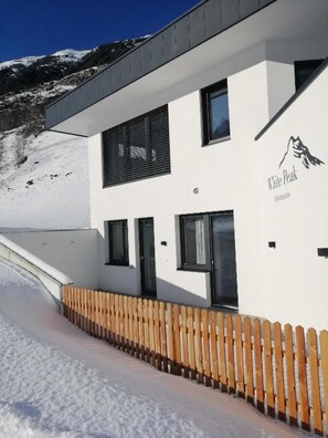 Un edificio moderno con fachada blanca, un logotipo que muestra una montaña y una valla de madera.