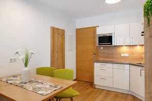 Una cocina compacta con armarios blancos, horno integrado y zona de comedor con mesa de madera y sillas verdes.
