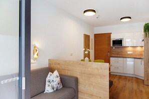 Una sala moderna con un sofá, un separador de madera y una cocina con armarios blancos y un microondas.