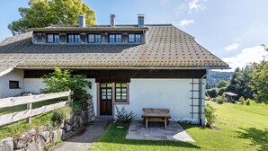 Une maison avec un toit en pente, une clôture en bois, un banc et un mur en pierre.