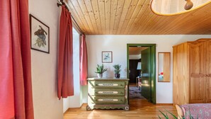 Une pièce avec un plancher en bois, une commode verte à tiroirs, un lit et une porte donnant sur une autre pièce.