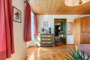 Une pièce avec un plancher en bois, une commode verte à tiroirs, un lit et une porte donnant sur une autre pièce.