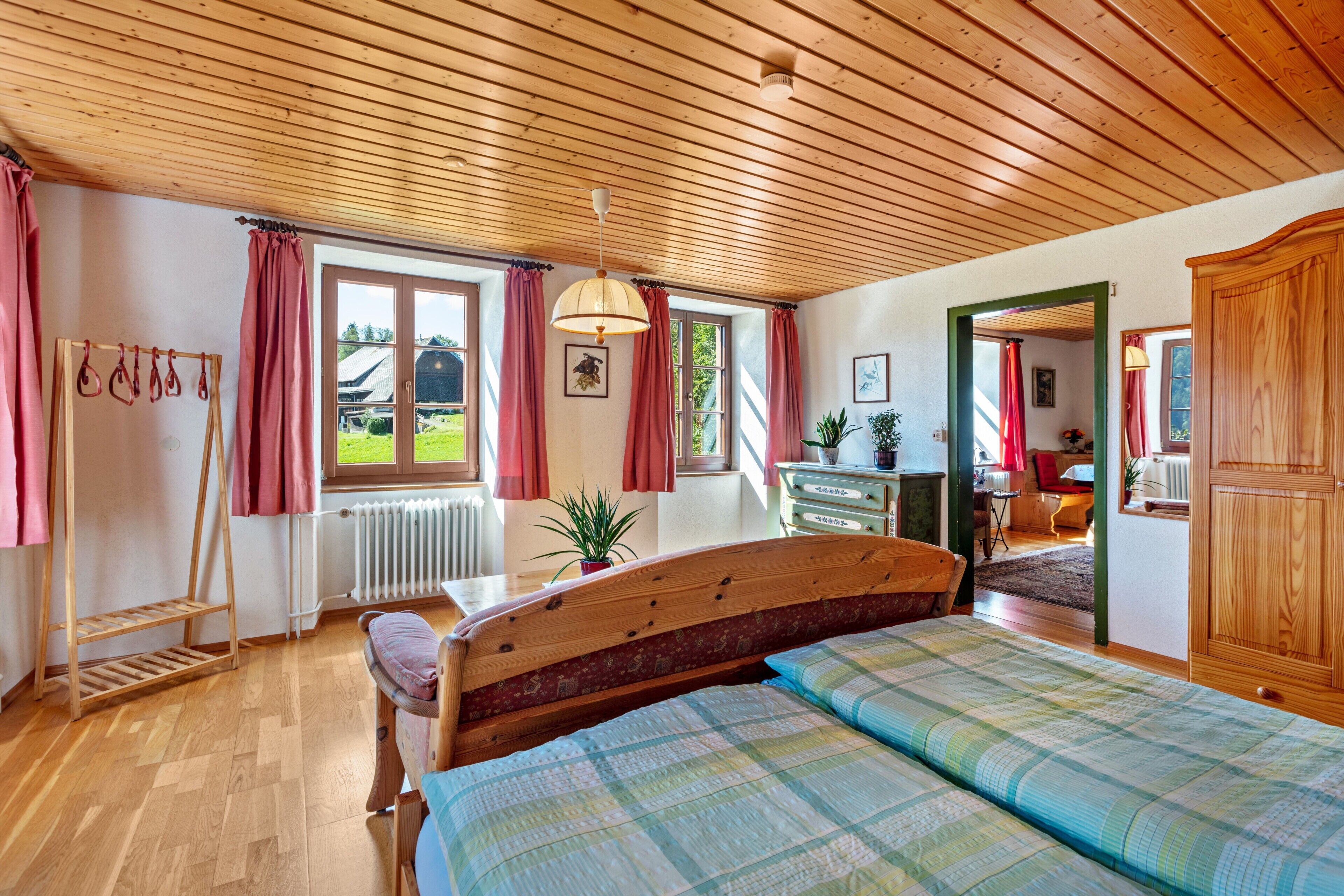 Un dormitorio con techo de madera, una cama con colcha, un aparador de madera, un radiador y una ventana con cortinas.