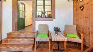 Une pièce avec un plancher en bois, deux chaises dotées de coussins verts, une petite table sur laquelle est posé un vase de fleurs et une fenêtre donnant sur un paysage.