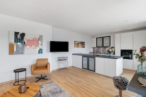 A modern kitchen with white cabinets, a central island, and a flat-screen TV mounted on the wall.