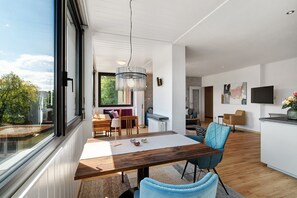 A modern kitchen with a dining area, large windows, and a view of the outdoors.