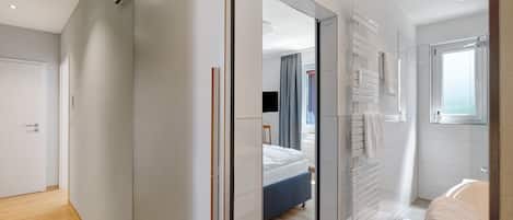 A modern hotel room with a wooden floor, a bed, a bathroom with a bathtub, and a large window.