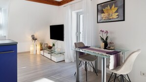 Uma sala de estar moderna com uma mesa de jantar de vidro, um sofá, uma TV e um quadro.