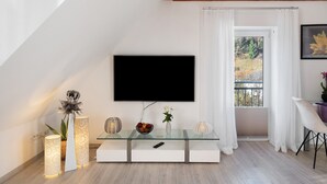 Uma sala de estar moderna com uma televisão de tela plana na parede, uma mesa de centro de vidro e um vaso com planta.