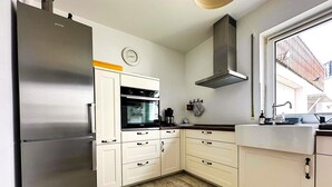 Een keuken met een roestvrijstalen koelkast, een oven, een afzuigkap en een raam met uitzicht op gebouwen.