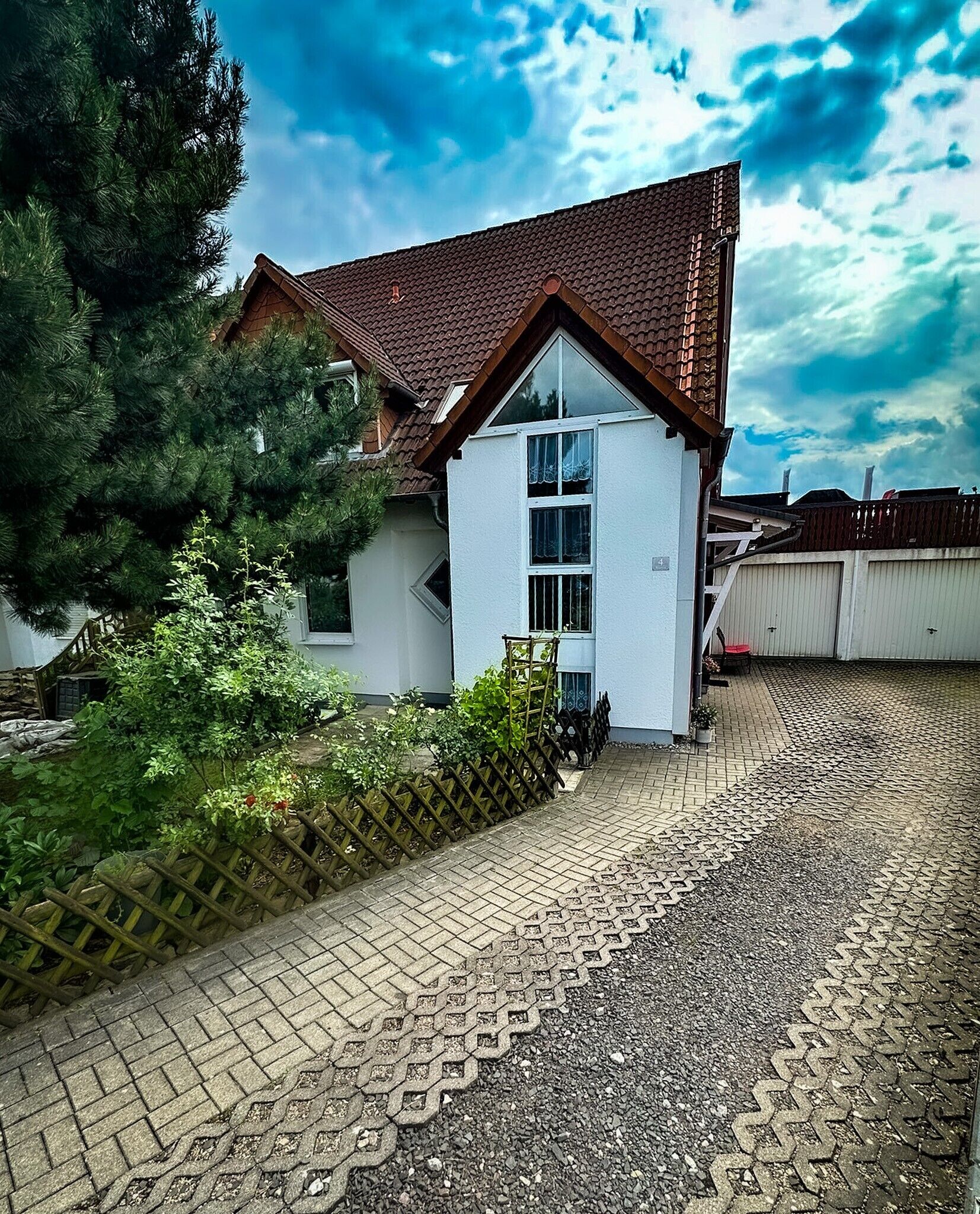 A house with a tiled roof, a white exterior, and a paved driveway leading to the entrance.