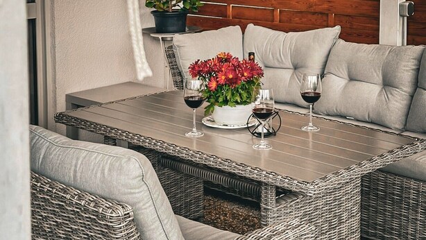 Een rieten tafel met twee kussens, een plant in pot en twee wijnglazen.