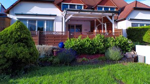 Een tweelaags huis met een overdekt terras, een omheinde tuin en een verzorgd gazon.