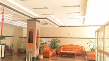 A lobby with a reception desk, a seating area with a sofa and armchairs, and a large potted plant.