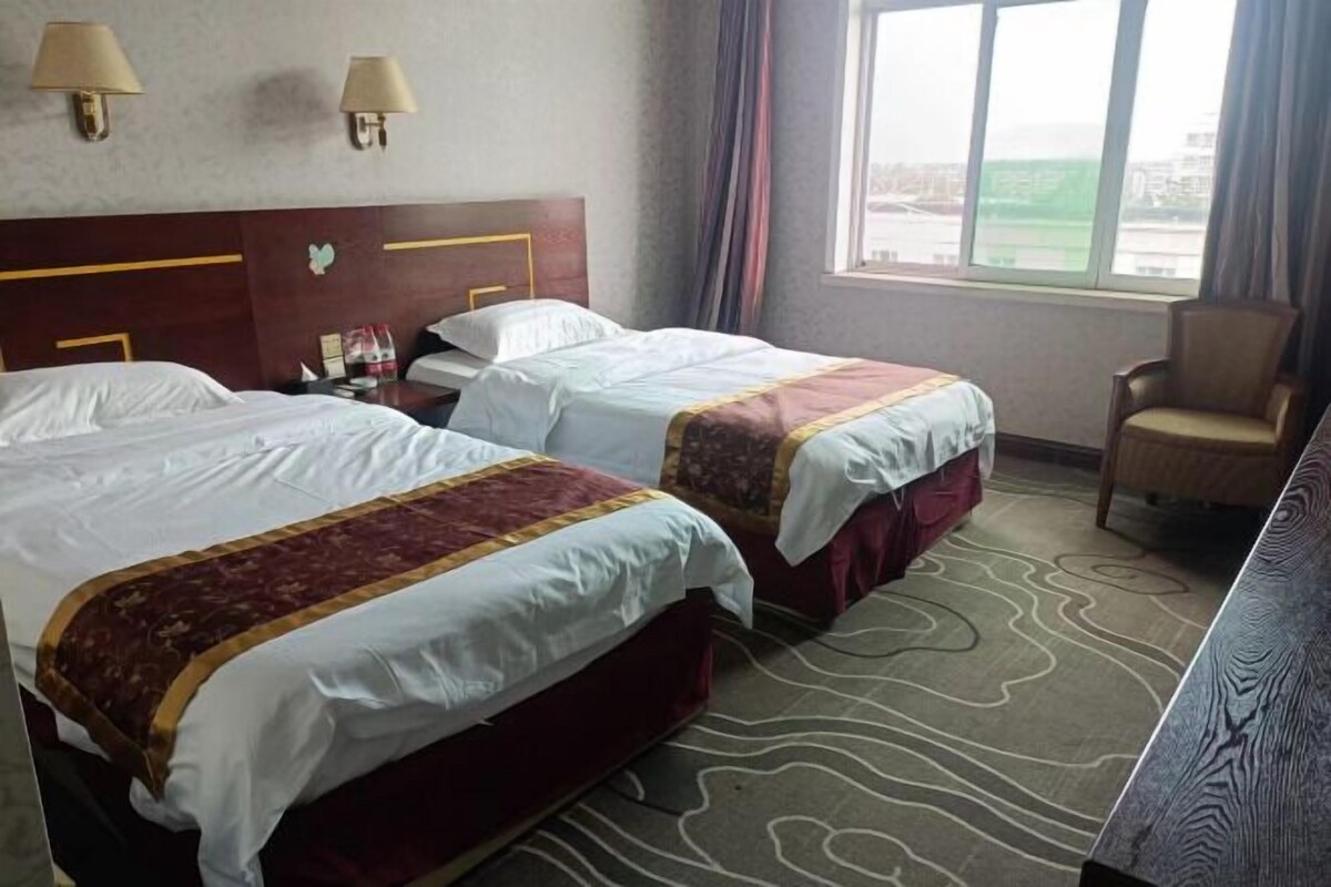 Une chambre d’hôtel avec deux lits, une tête de lit, des lampes, une chaise et une vue sur l’extérieur.