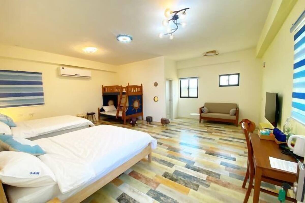 A hotel room with two beds, a sofa, a dining table, and a TV.