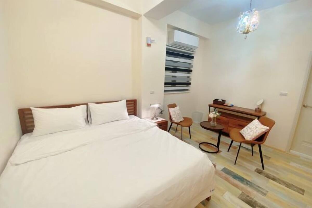 A bedroom with a bed, a desk, two chairs, and a small table.