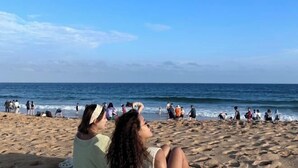 A beach with people walking and sitting on the sand, and the ocean in the background.
