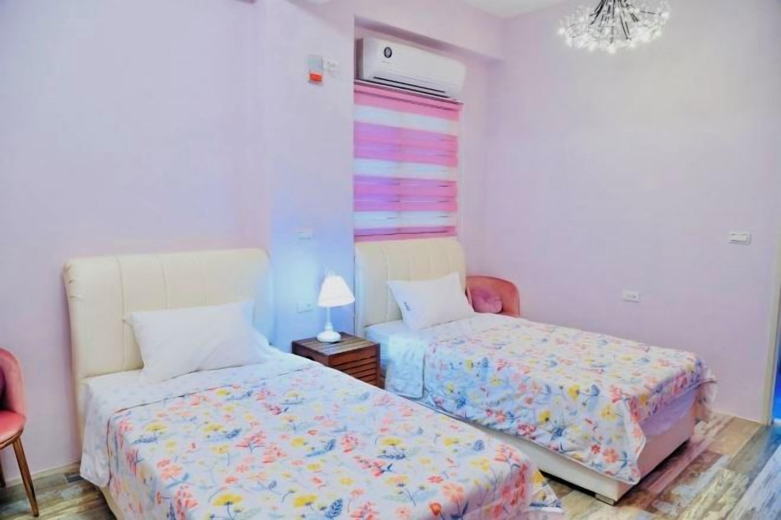 A bedroom with two beds, a nightstand, a lamp, and an air conditioning unit.