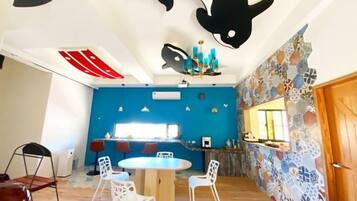 A room with a blue accent wall, a round dining table with chairs, a kitchen area with a window, and a patterned wall.