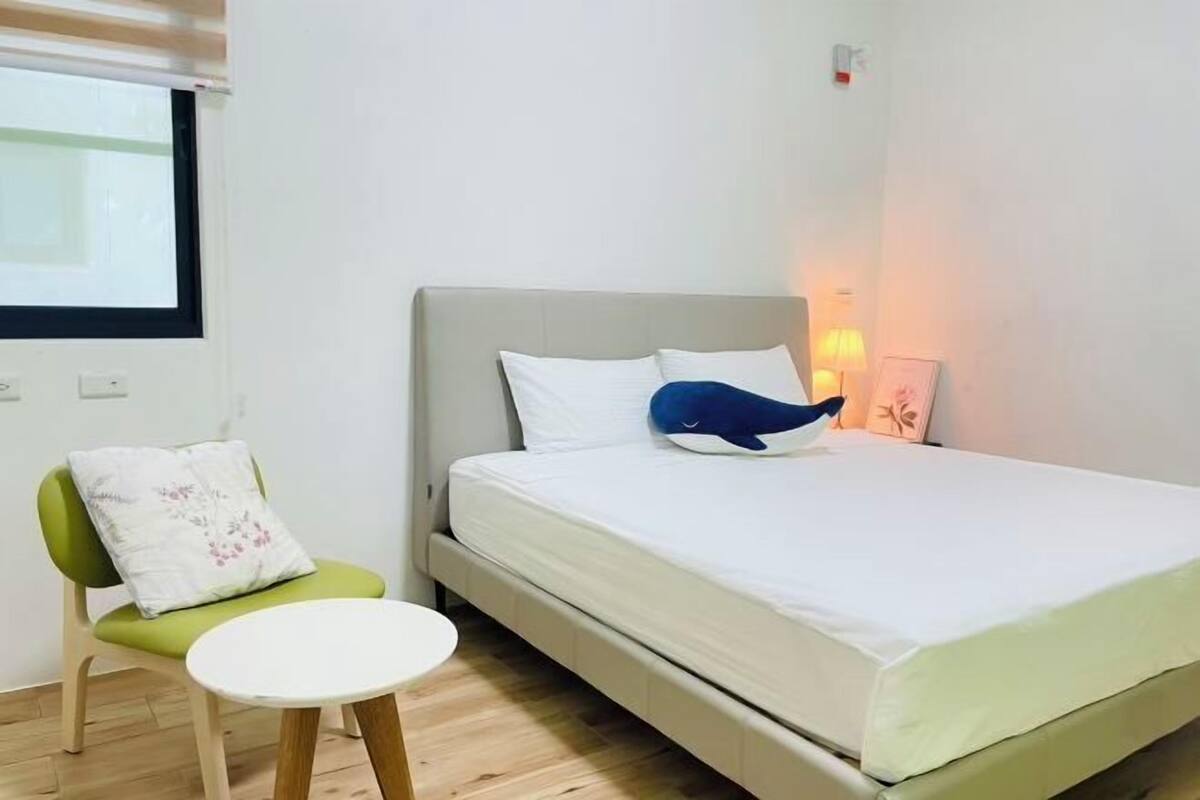 A bedroom with a bed, a chair, a small table, and a bedside lamp.