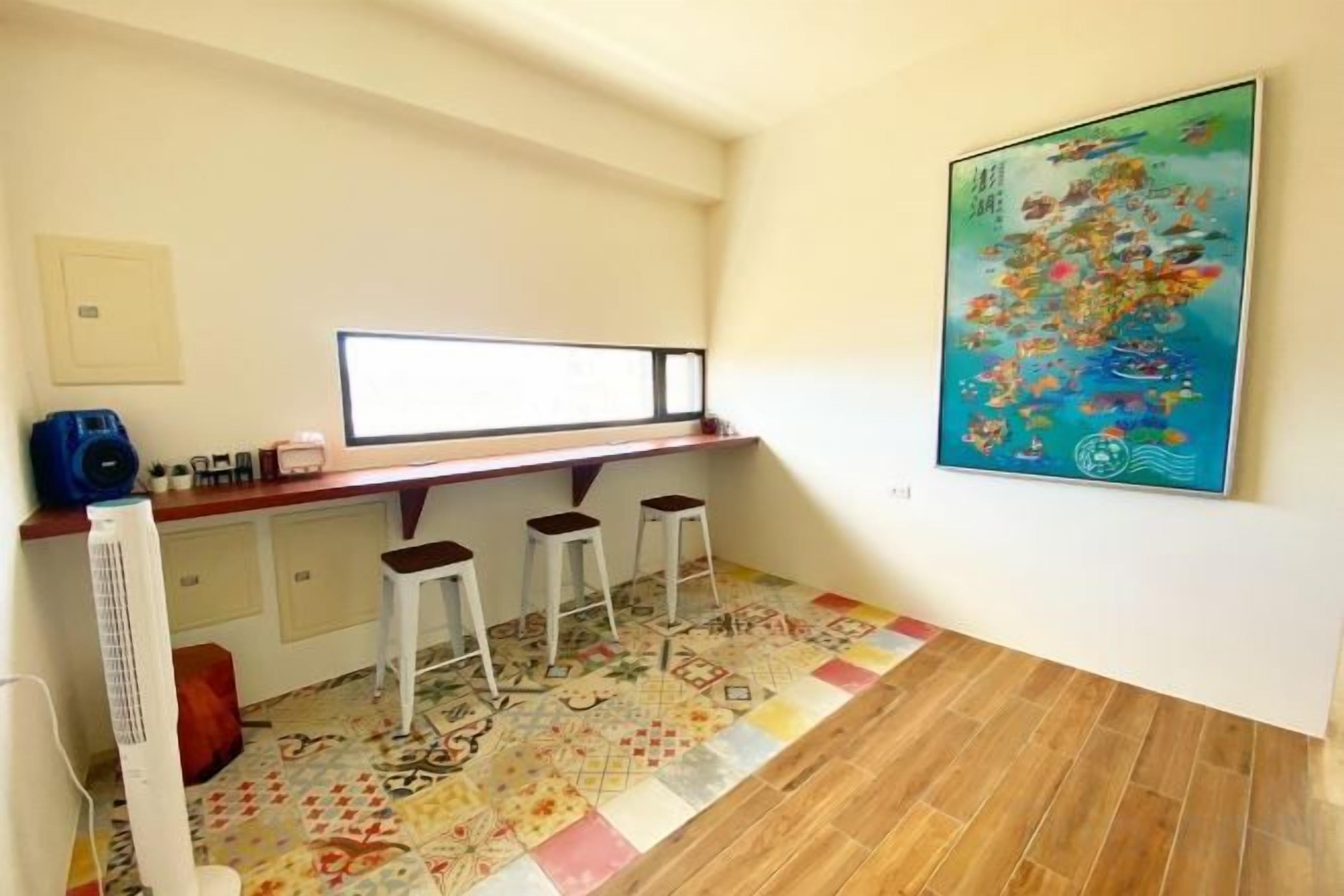 A room with a desk, two stools, a radiator, a patterned floor, and a painting on the wall.
