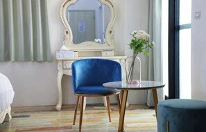 A hotel room with a blue chair, a round table, a white dresser with a mirror, and a vase with flowers. - CAMINO B&B (Penghu)