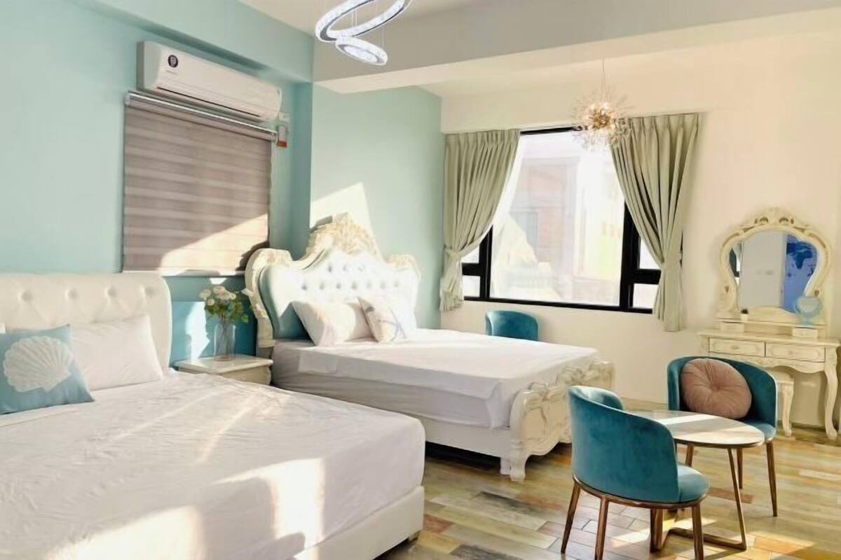 A bedroom with two beds, a desk, a chair, and a window with curtains.