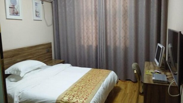 A hotel room with a bed, a desk with a computer, and a window with curtains.