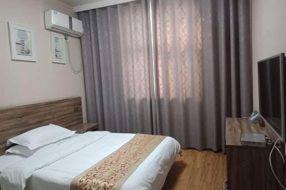 A hotel room with a bed, curtains, a TV, and an air conditioning unit.