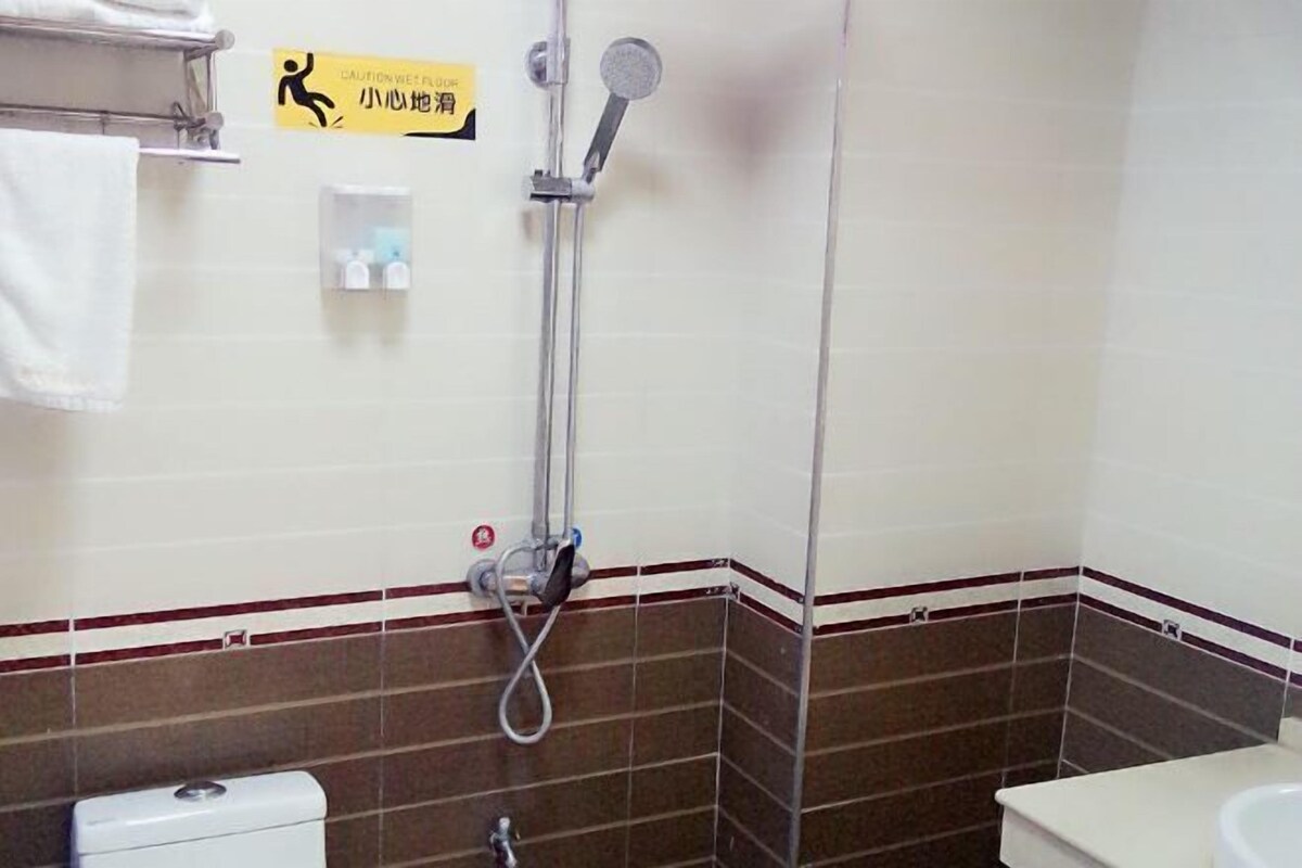 A bathroom with a shower, toilet, and sink. There's a caution sign on the wall.